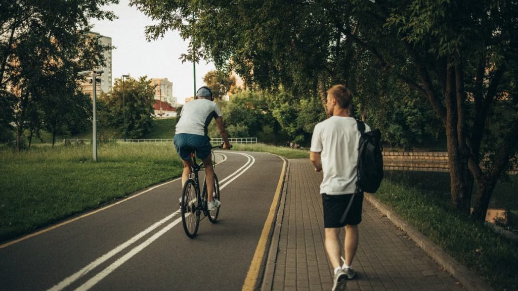 A cyclist and a walker enjoy a peaceful park trail surrounded by greenery.